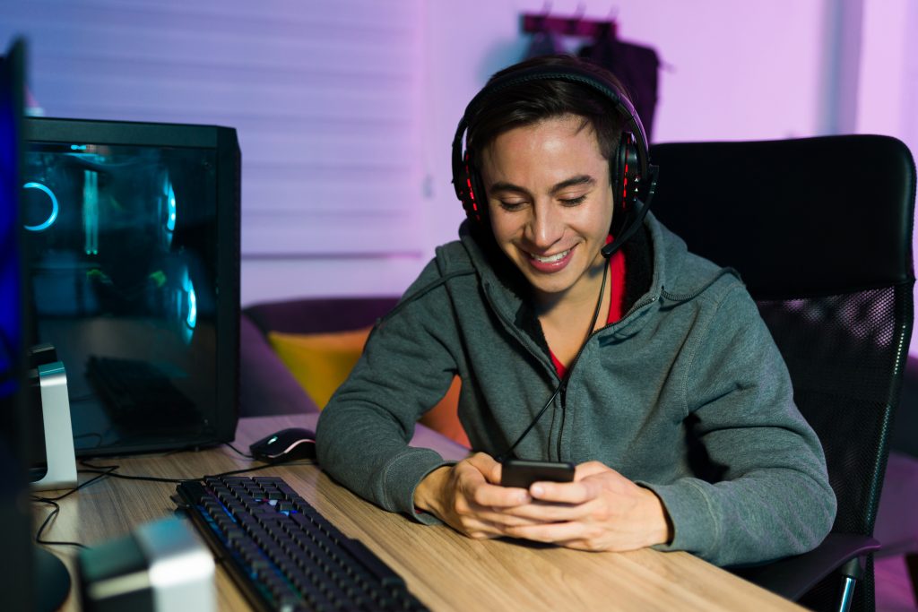 Jovem jogador de videogame online checando promoções por SMS em seu smartphone durante uma sessão de jogo no Brasil