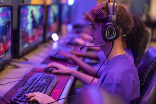 Jogador de videogame online usando headset e computador em um setup gamer, focado na interação em tempo real do jogo