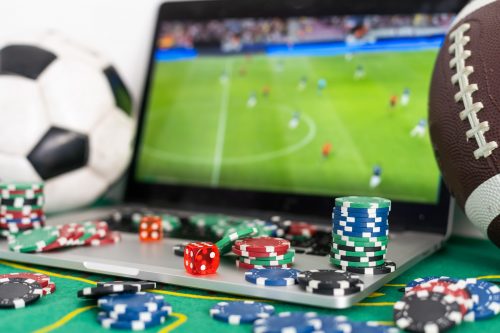 Fichas de cassino e dados ao lado de um laptop exibindo uma partida de futebol para plataformas de jogos online.